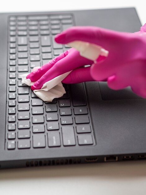 Hoge hoek van handen met chirurgische handschoenen die laptop oppervlak schoonmaken