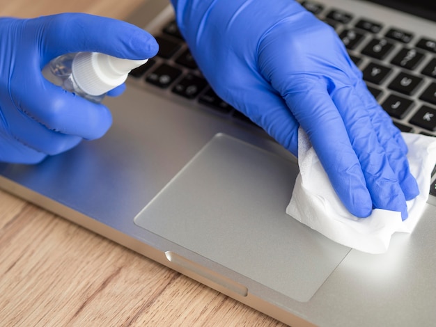 Hoge hoek van handen met chirurgische handschoenen die laptopoppervlak desinfecteren