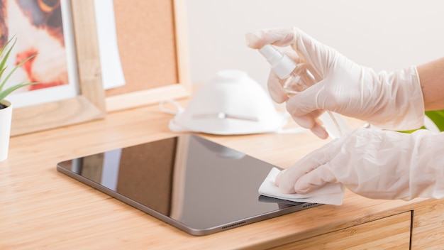 Hoge hoek van handen met chirurgische handschoenen die tablet op bureau desinfecteren