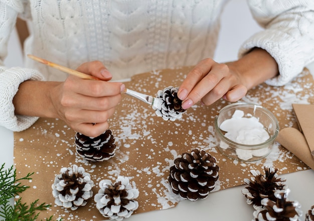 Gratis foto hoge hoek van persoon schilderij dennenappels voor kerstmis