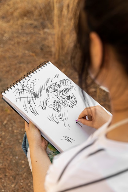 Hoge hoek van vrouwelijke schilder buitenshuis schetsen op laptop