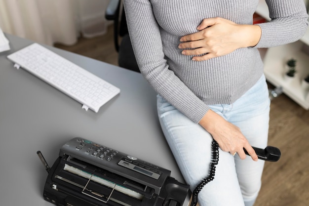 Hoge hoek van zwangere zakenvrouw met telefoon op kantoor
