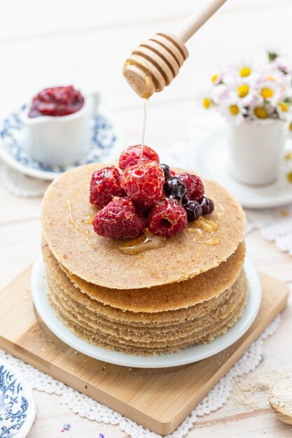 Hoge hoek verticale close-up shot van rauwe veganistische pannenkoeken met honing en bessen