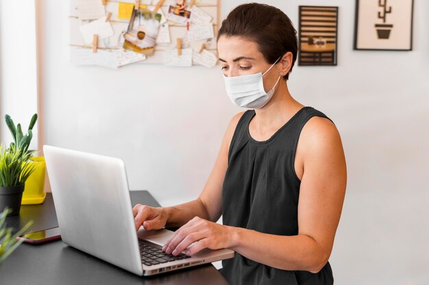 Hoge hoek vrouw met masker die op laptop werkt