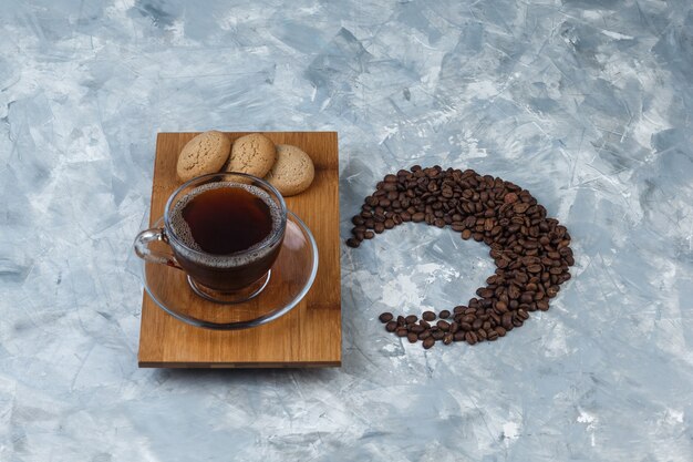 Hoge hoek weergave kopje koffie, koekjes op houten snijplank met koffiebonen op lichtblauwe marmeren achtergrond. horizontaal