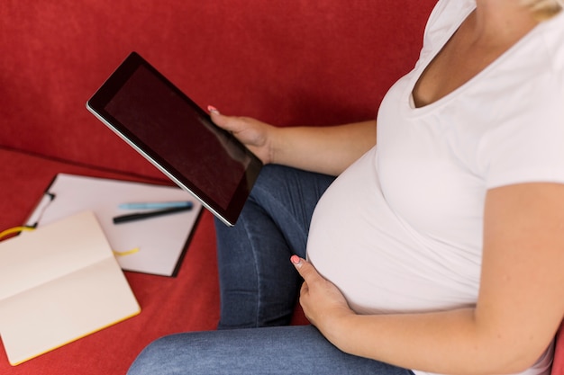 Gratis foto hoge hoek zwangere vrouw die op haar tablet kijkt