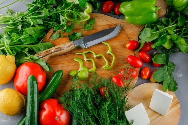 Hoge hoekmening gesneden groene paprika op snijplank met tomaten, zout, kaas, citroen, groenen, mes op grijze ondergrond