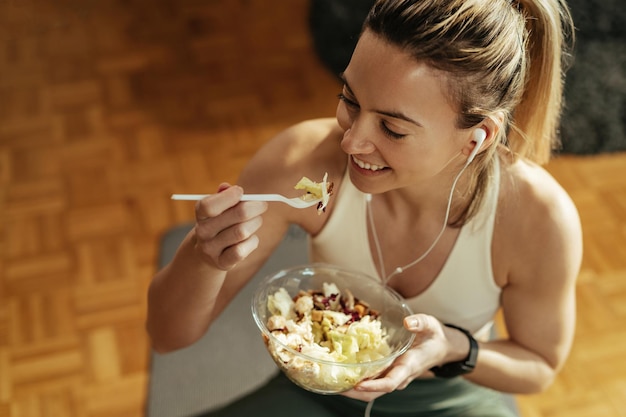 Hoge hoekmening van atletische vrouw die geniet van een gezonde salade na sporttraining thuis