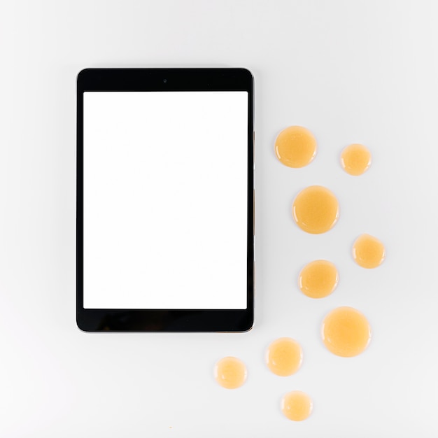 Hoge hoekmening van digitale tablet en druppel honing op witte achtergrond