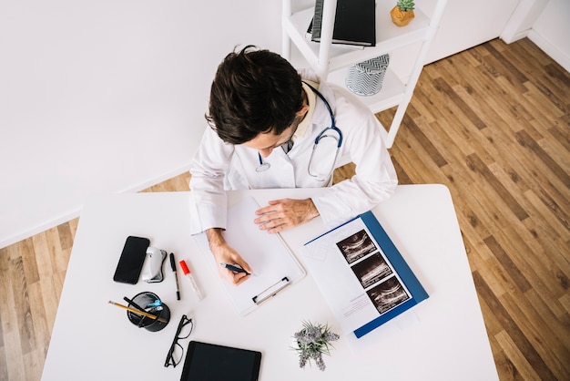 Hoge hoekmening van een mannelijke arts die op klembord in kliniek schrijft