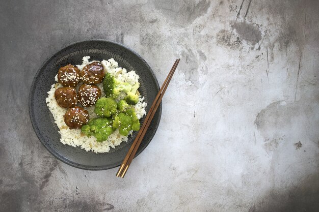 Hoge hoekmening van gekookte rijst met gehaktballen en broccoli in een plaat op tafel met stokjes