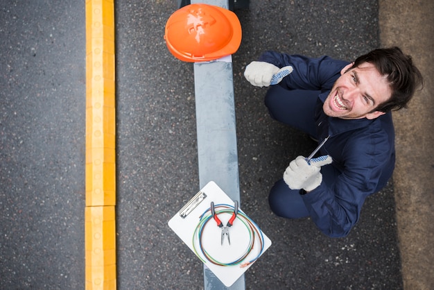 Hoge hoekmening van gelukkige mannelijke elektricien die duim op het werk tonen