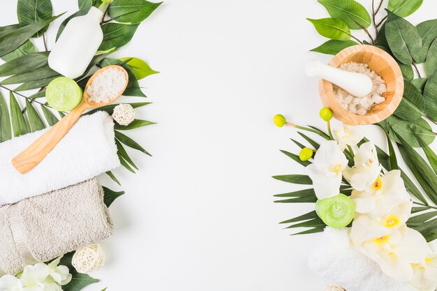 Hoge hoekmening van handdoeken; zout; kaarsen; bloemen en bladeren op whit oppervlak