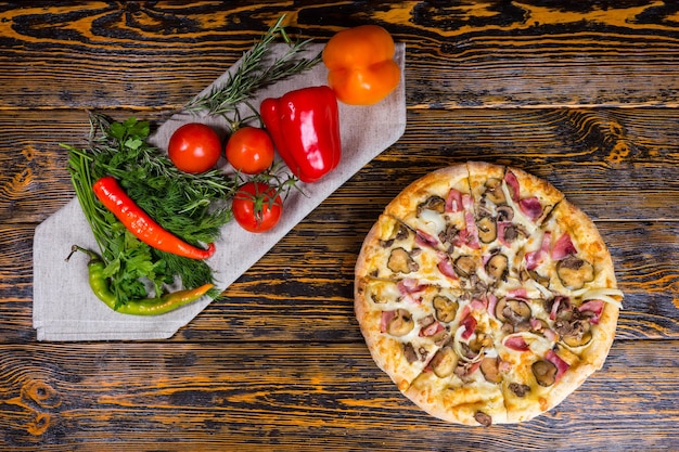 Hoge hoekmening van heerlijke pizza met ham, champignons, ui en augurken in de buurt van zijn paprika's, tomaten en andere groenten op een servet op houten tafel