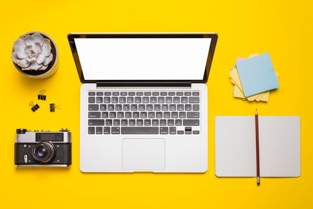 Hoge hoekmening van laptop; camera; stationeries en vetplant op geel oppervlak