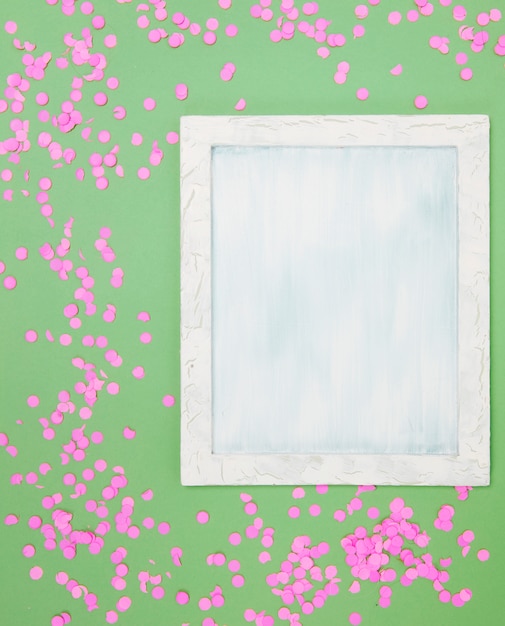 Hoge hoekmening van leeg frame met roze confetti tegen een groene achtergrond