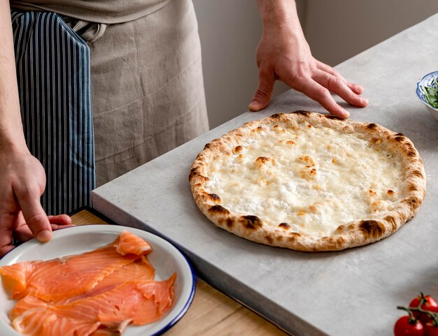 Hoge hoekmens die zich dichtbij gebakken pizzadeeg en gerookte zalmplakken bevindt