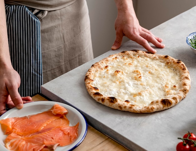 Hoge hoekmens die zich dichtbij gebakken pizzadeeg en gerookte zalmplakken bevindt