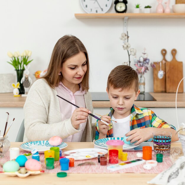 Hoge hoekmoeder die zoon helpt om eieren te schilderen