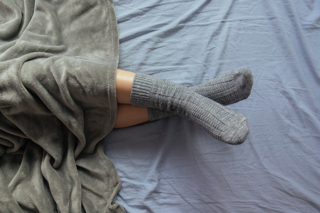 Hoge hoekopname van de benen van een vrouw in grijze gebreide sokken onder de deken