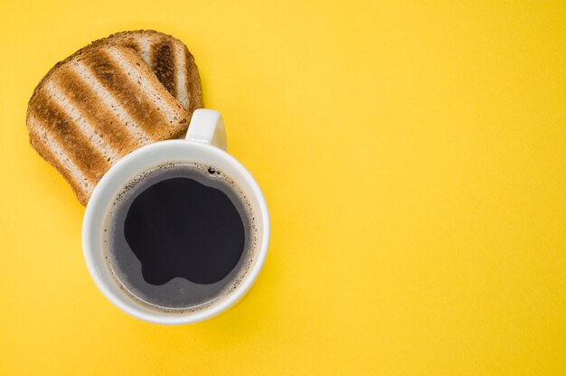 Hoge hoekopname van een kopje koffie en toast op een geel oppervlak