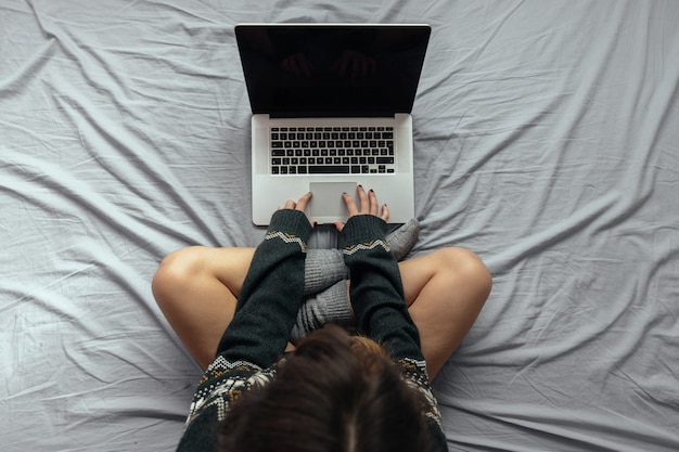 Hoge hoekopname van een vrouw die op de laptop typt terwijl ze met gekruiste benen op het bed zit