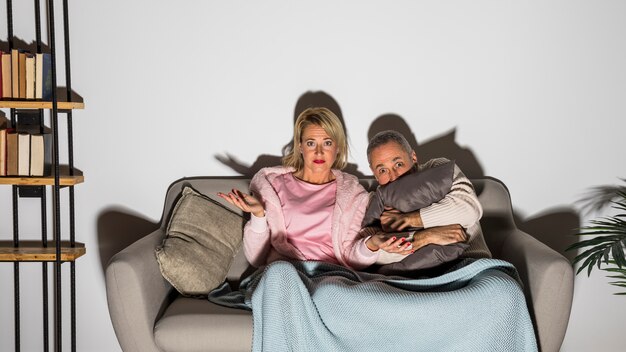 Hogere doen schrikken man dichtbij verraste vrouw die op TV op sofa letten