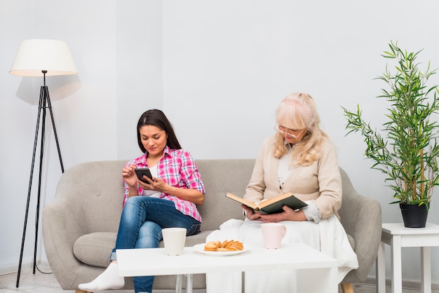 Hogere het boekzitting van de moederlezing dichtbij haar dochter die mobiele telefoon met ontbijt op lijst met behulp van