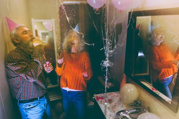 Hogere man die de partijhoorn en de vrouw blaast die confettien in de lucht op verjaardag werpen