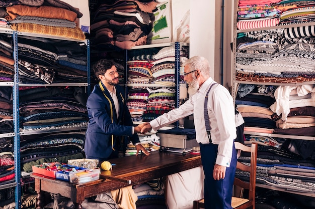 Hogere mannelijke klant het schudden handen met jonge mannelijke kleermaker in zijn workshop