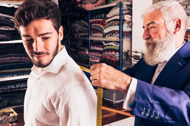 Hogere mannelijke manierontwerper die meting van zijn klant in de winkel neemt