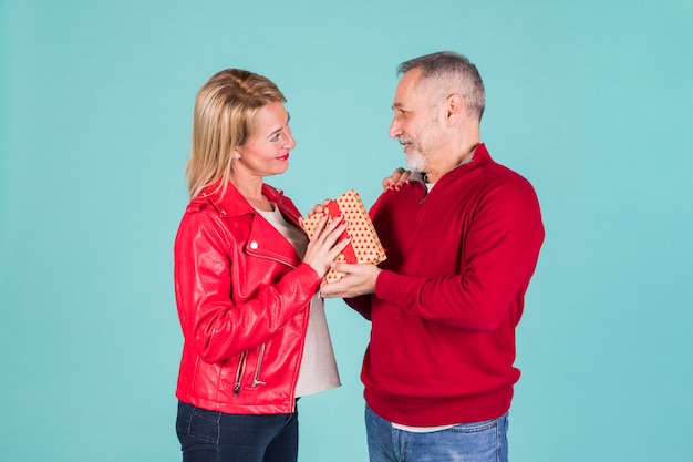 Gratis foto hogere mens die heden geeft aan zijn vrouw die zich tegen blauwe achtergrond bevindt