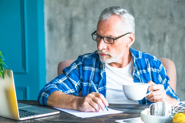 Hogere mens die laptop holdingspen bekijken die nota&#39;s maken