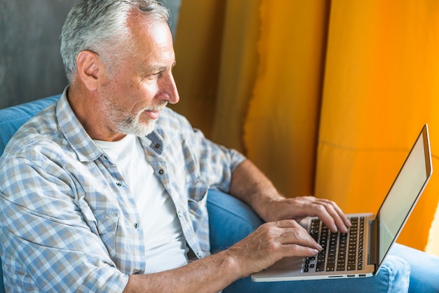 Hogere mensenzitting op bank die laptop met behulp van