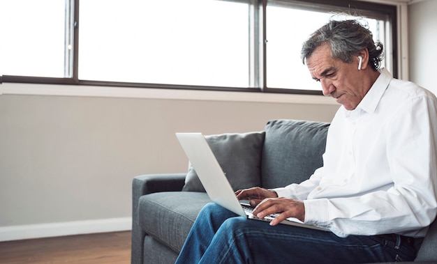 Hogere mensenzitting op bank die laptop met behulp van