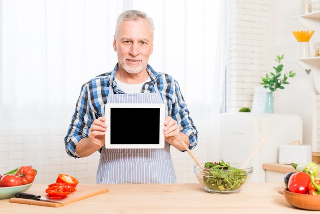 Hogere vrouw die de plantaardige salade voorbereiden door mobiele telefoon te bekijken