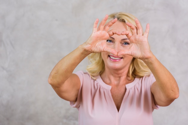 Hogere vrouw die een hart met haar vingers maakt