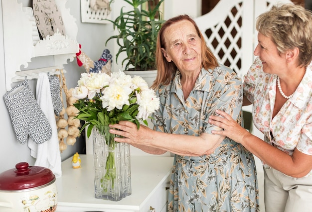 Gratis foto hogere vrouw die witte bloemvaas houdt die zich dichtbij haar dochter bevindt