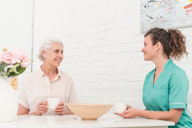 Hogere vrouw en vrouwelijke verpleegster die koffie hebben samen