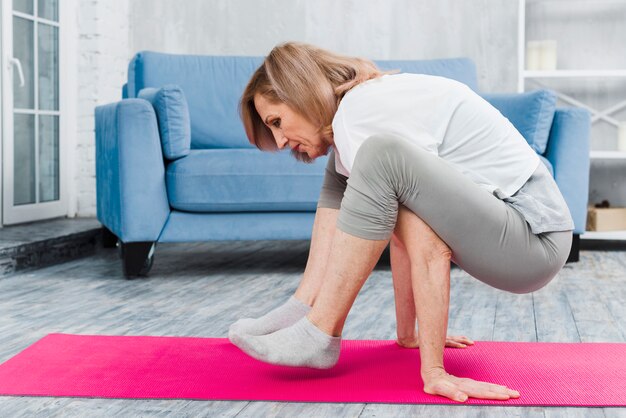 Hogere vrouw het praktizeren yoga thuis