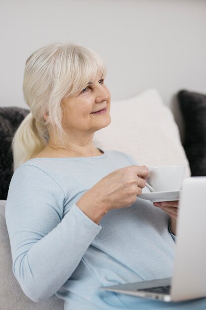 Hogere vrouw met hete drank en laptop