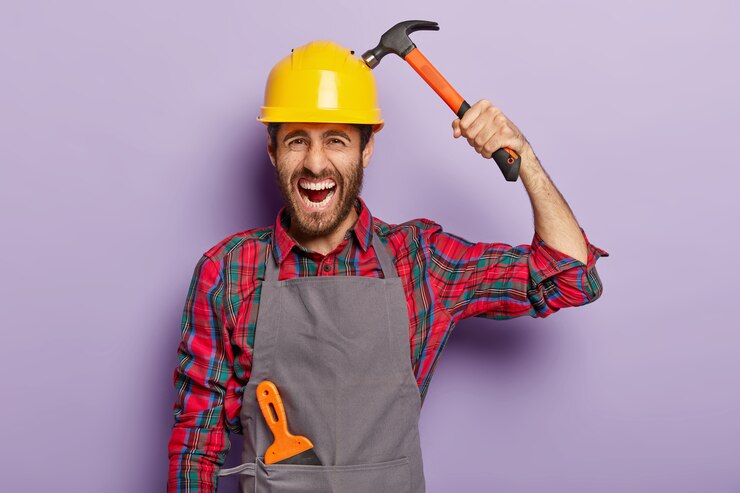 Gratis Foto home verbetering, reparatie, bouwen en repareren concept. geërgerd voorman draagt helm en houdt hamer vast, bezig met werken in werkplaats, schreeuwt negatief. ervaren mannelijke ingenieur gebruikt bouwgereedschap