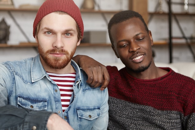 Gratis foto homoseksualiteit, interraciale relaties, liefde en geluk concept. mannelijke partners van samesex brengen samen leuke tijd door in de coffeeshop, zitten dicht bij elkaar en praten over hun toekomst