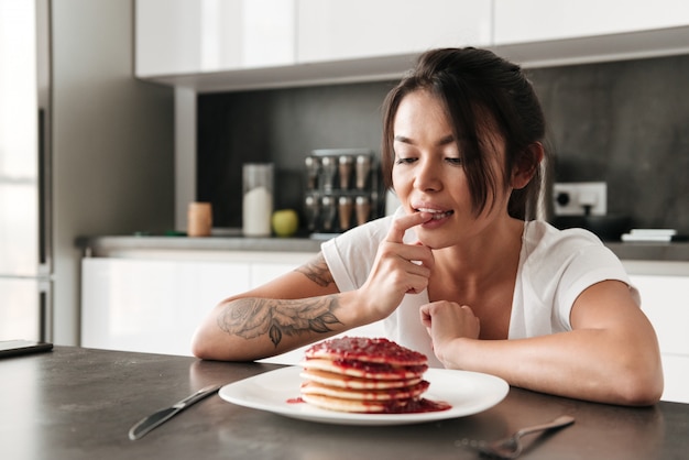 Hongerige jonge vrouwenzitting bij de keuken in huis