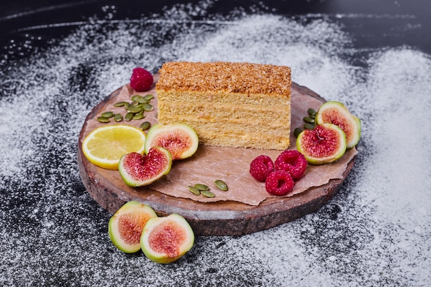 Honingcake versierd met vijgen, bessen en schijfje citroen in het midden van de donkere tafel.