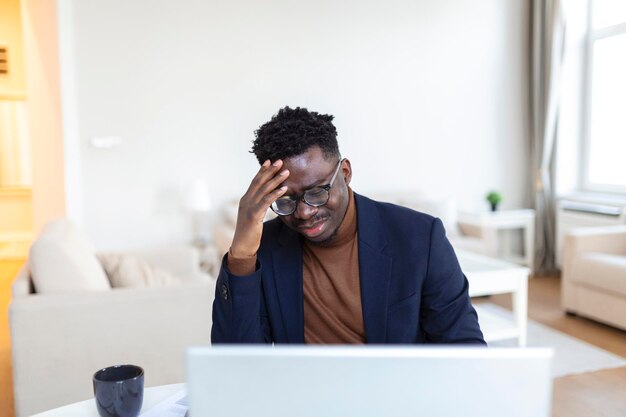 Hoofd geschoten gestresste jonge Afro-Amerikaanse man die voorhoofd aanraakt en lijdt aan vreselijke hoofdpijn die op de computer in het kantoor aan huis werkt Gefrustreerde verwarde biraciale man met pijnlijke gevoelens in het hoofd