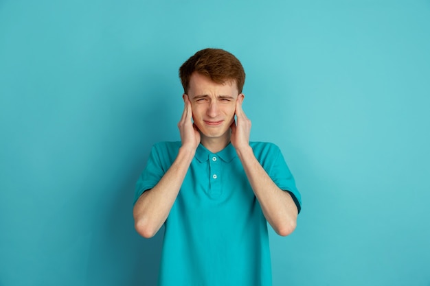 Hoofdpijn, boos. Het moderne portret van de blanke jongeman geïsoleerd op een blauwe muur, zwart-wit. Mooi mannelijk model.