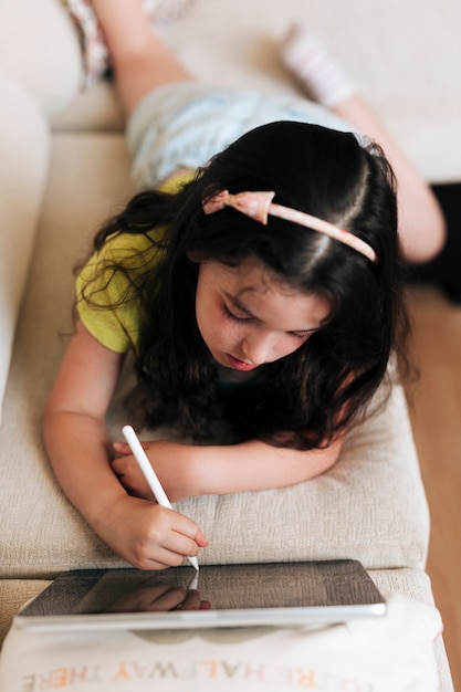 Hoog hoekmeisje dat op de bank met haar tablet legt