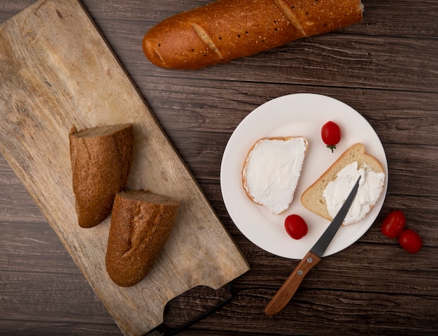 Hoogste mening van besnoeiing in half stokbrood en witte broodplakken met tomaten en mes in plaat op houten achtergrond