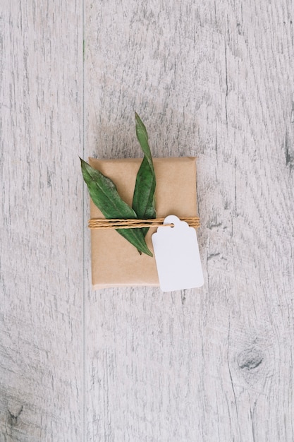 Gratis foto hoogste mening van bruine verpakte giftdoos met markering en groene bladeren op houten lijst